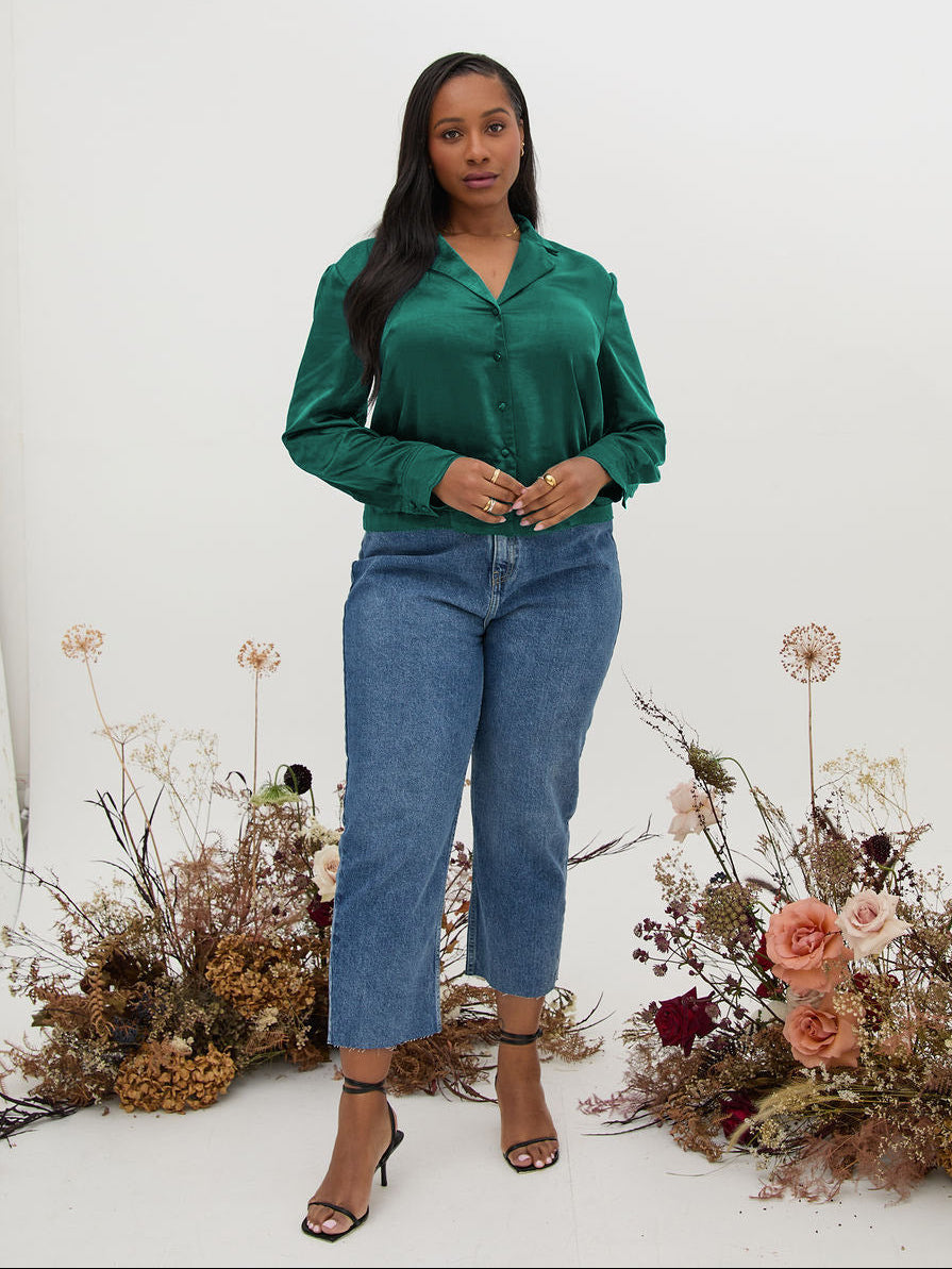 Woman wearing a green shirt and blue jeans standing in front of floral arrangements on a white background
