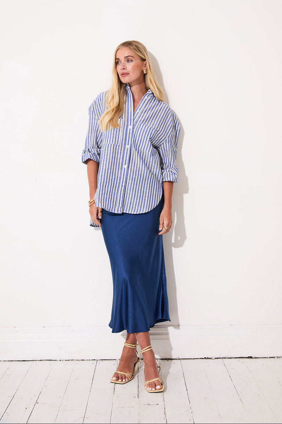 Woman wearing a blue and white striped shirt and navy skirt against a white wall.