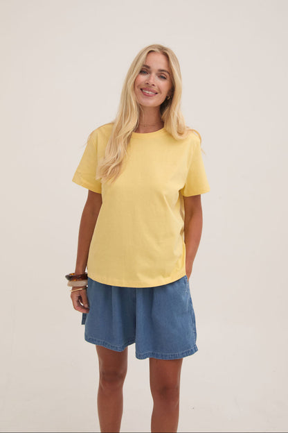 Woman wearing a yellow t-shirt and blue shorts on a plain background