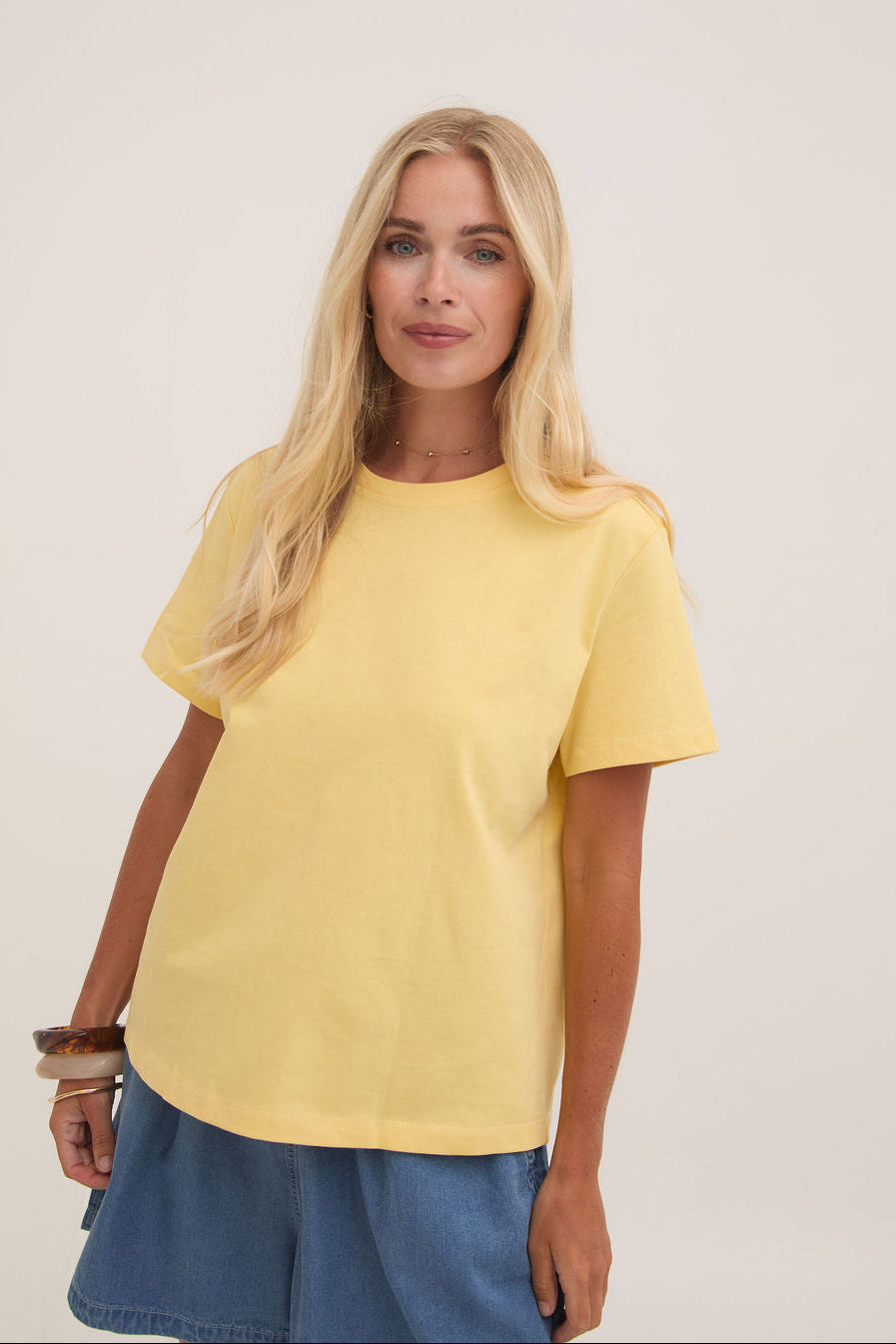 Woman wearing a yellow t-shirt and blue shorts on a plain background