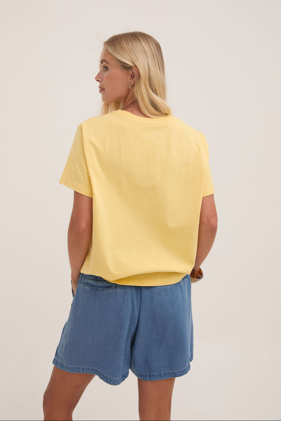 Woman wearing a yellow t-shirt and denim shorts on a plain background