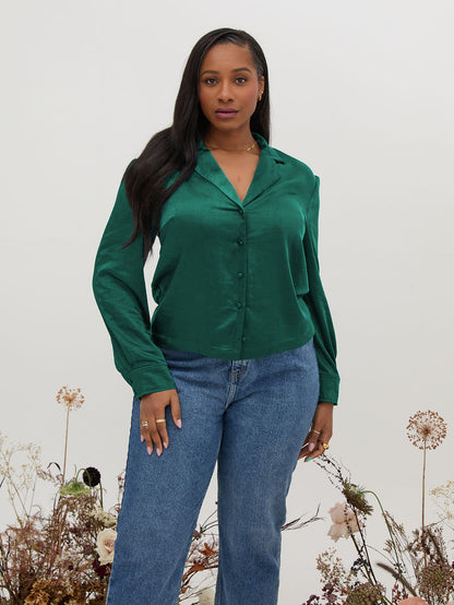 Woman wearing a green shirt and blue jeans standing against a white background with floral decorations.