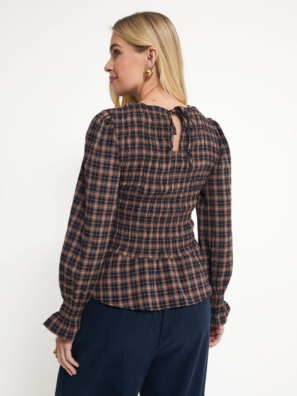 A woman shown from the back wearing a long-sleeve plaid top in dark brown and black with navy pants, photographed against a plain white studio background.