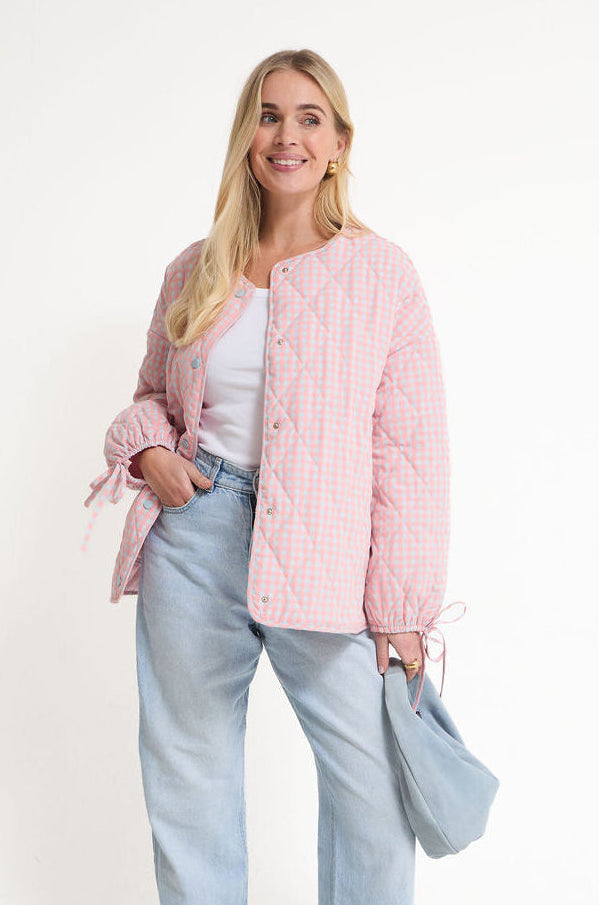Woman wearing a pink puffer jacket and light blue jeans on a white background
