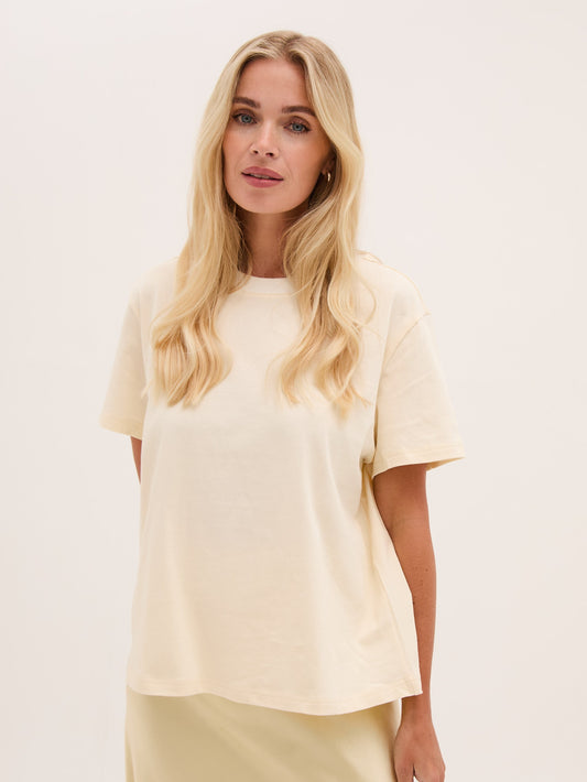 Woman wearing a cream t-shirt and yellow skirt against a plain background