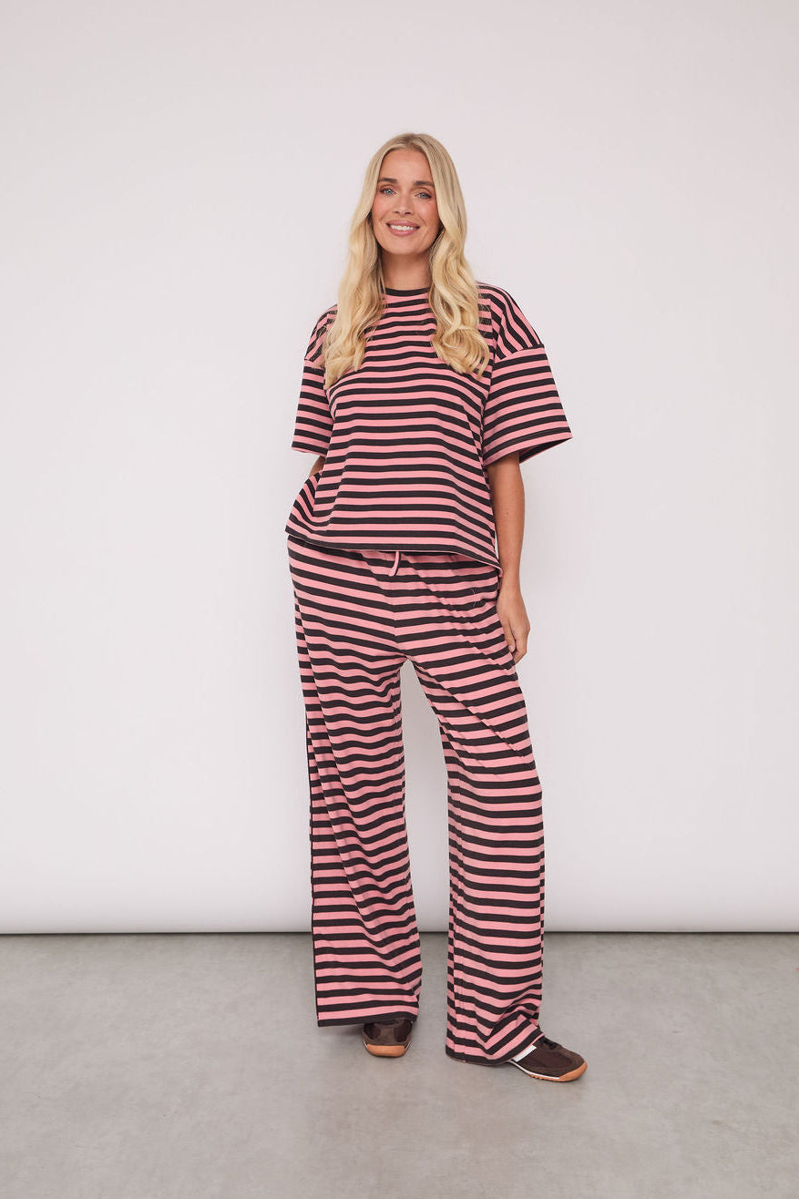 A woman modeling a matching two-piece loungewear set consisting of a short-sleeve top and wide-leg pants, both featuring horizontal dark red and beige stripes, set against a plain white studio background.