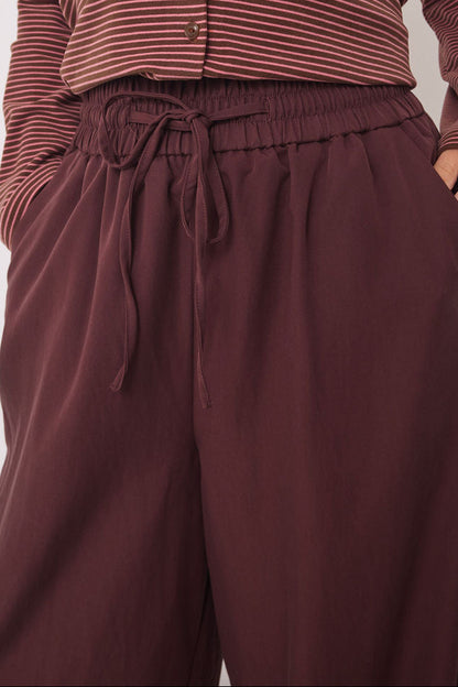 A woman wearing a ribbed long-sleeve cropped top in a muted burgundy and brown stripe pattern, paired with matching wide-leg drawstring pants, against a plain light gray background.
