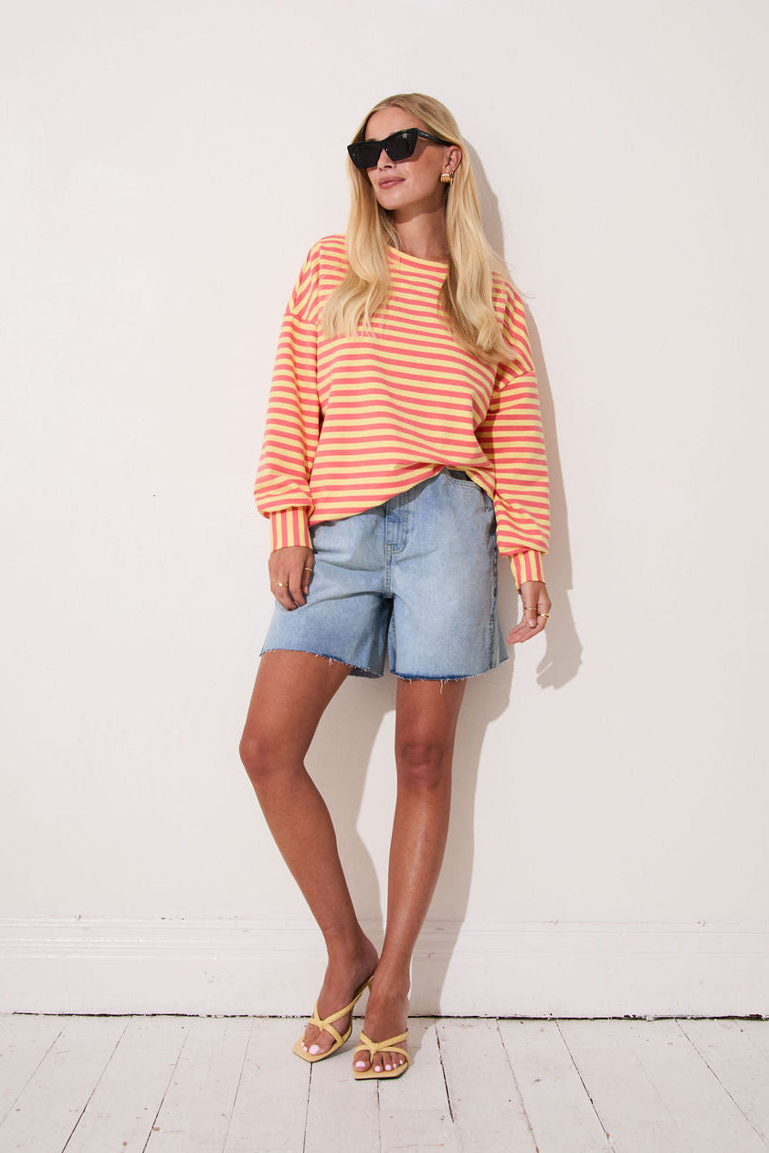 Woman wearing a striped sweater and denim shorts against a white background