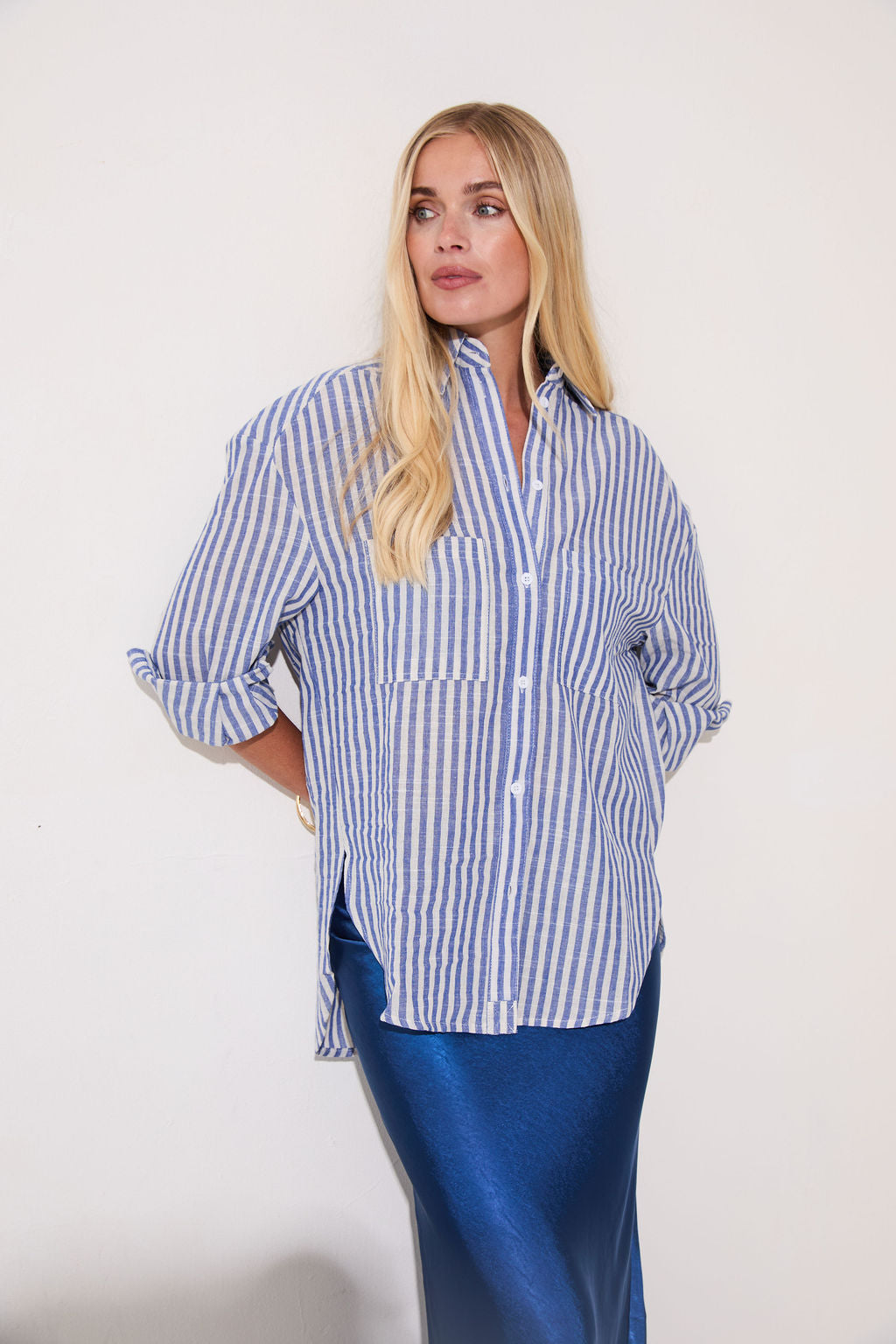 Woman wearing a blue and white striped shirt with rolled-up sleeves against a plain background
