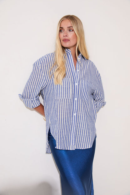 Woman wearing a blue and white striped shirt with rolled-up sleeves against a plain background