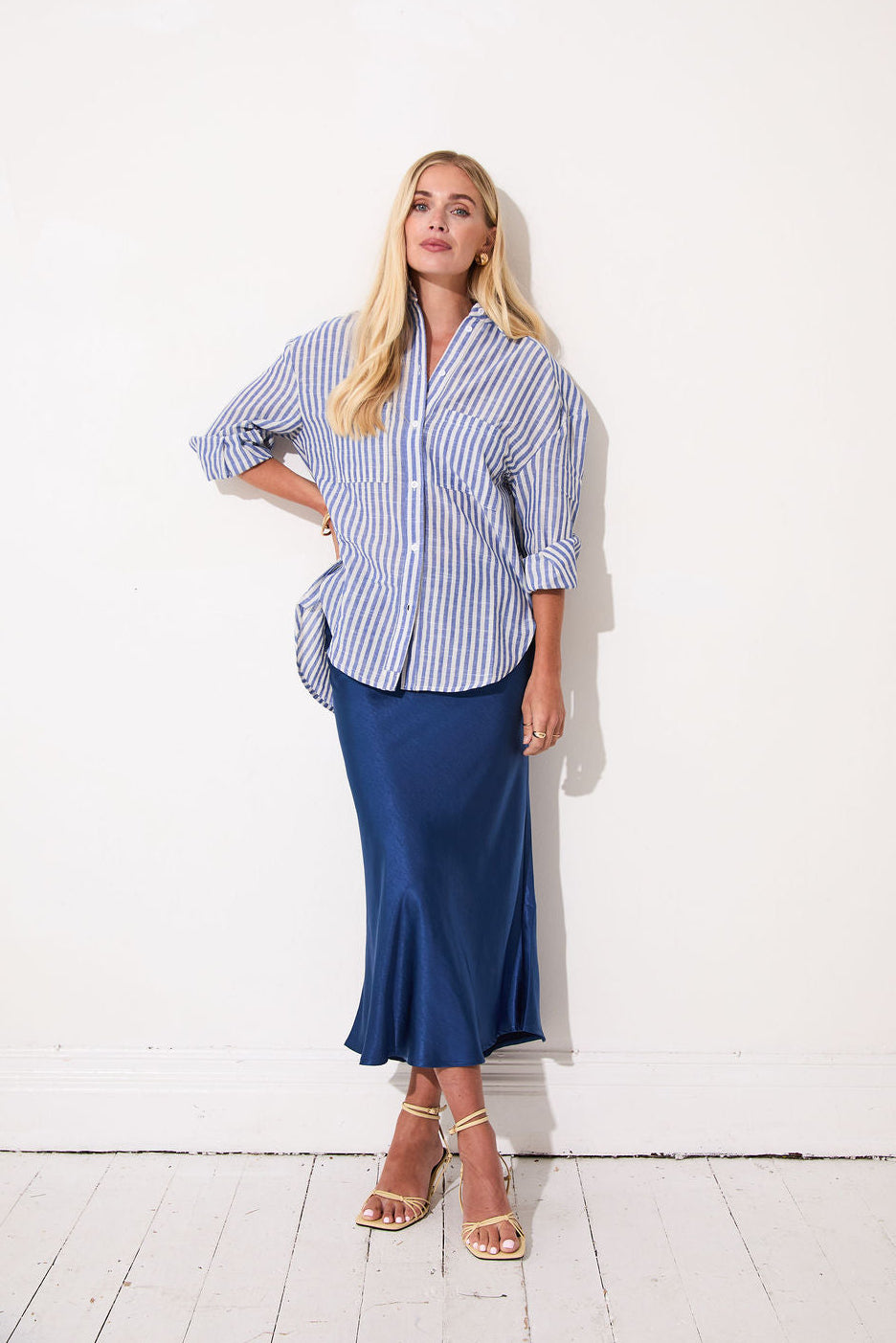 Woman wearing a blue and white striped shirt and blue skirt against a white wall.